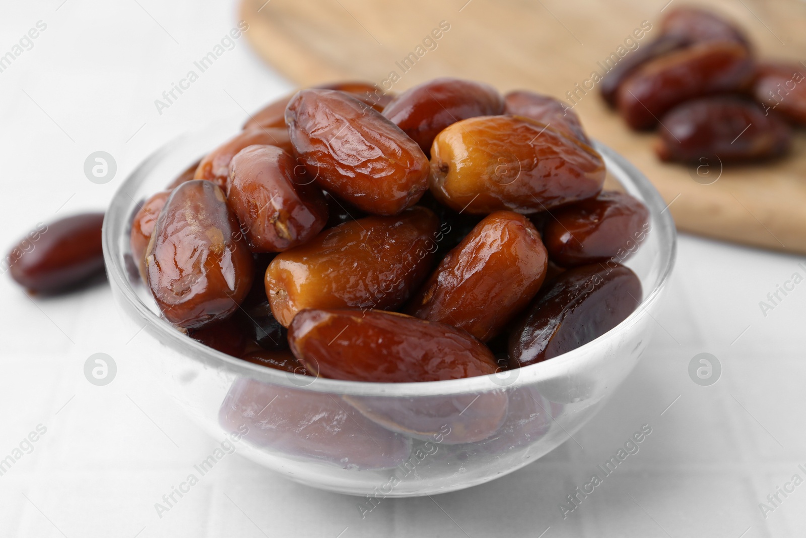 Photo of Tasty dried dates in glass bowl on white table, closeup