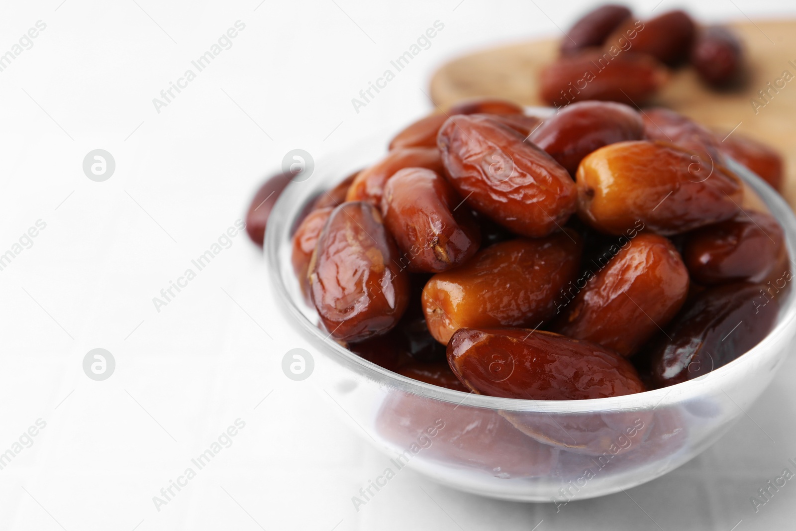 Photo of Tasty dried dates in glass bowl on white table, closeup. Space for text