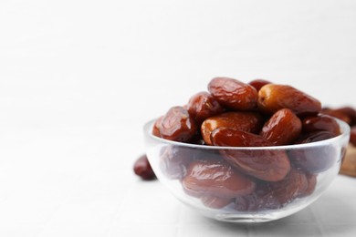 Photo of Tasty dried dates in glass bowl on white table, closeup. Space for text