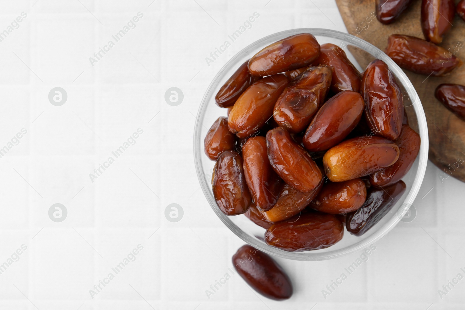 Photo of Tasty dried dates in glass bowl on white table, top view. Space for text