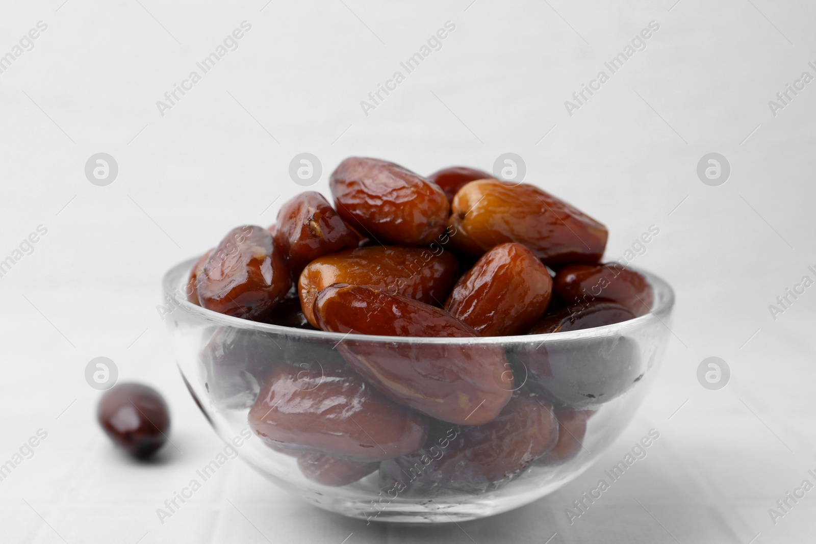 Photo of Tasty dried dates in glass bowl on white table, closeup