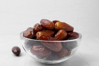 Photo of Tasty dried dates in glass bowl on white table, closeup