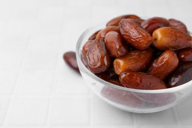 Photo of Tasty dried dates in glass bowl on white table, closeup. Space for text