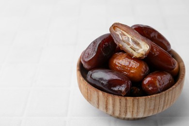 Photo of Tasty dried dates in bowl on white table, closeup. Space for text