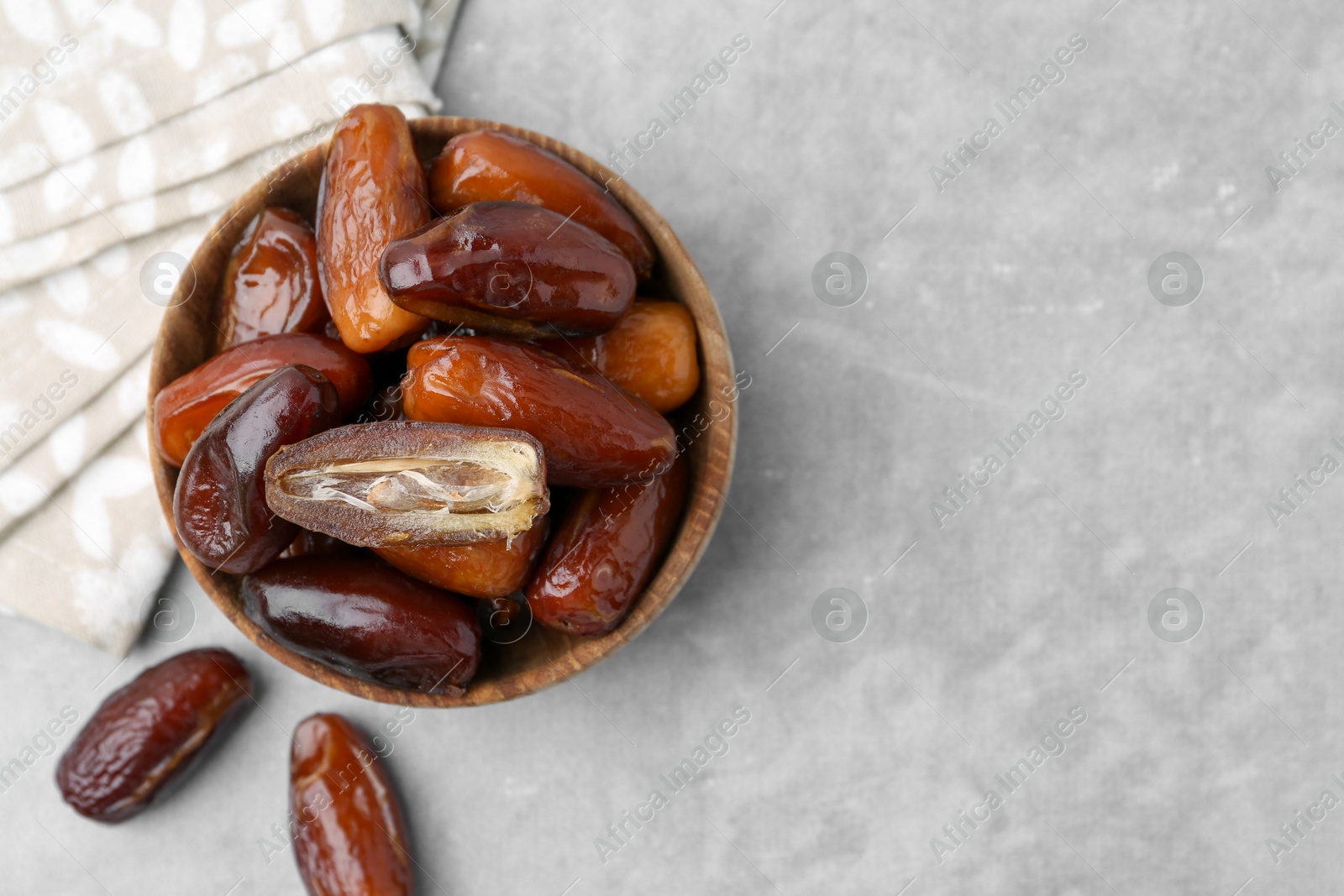 Photo of Tasty dried dates in bowl on light grey table, top view. Space for text