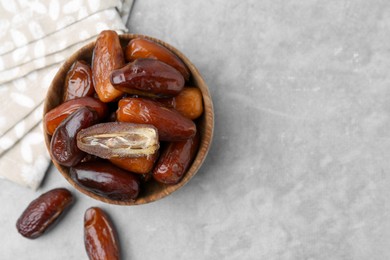 Photo of Tasty dried dates in bowl on light grey table, top view. Space for text