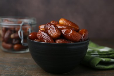 Photo of Tasty dried dates in bowl and jar on wooden table, closeup