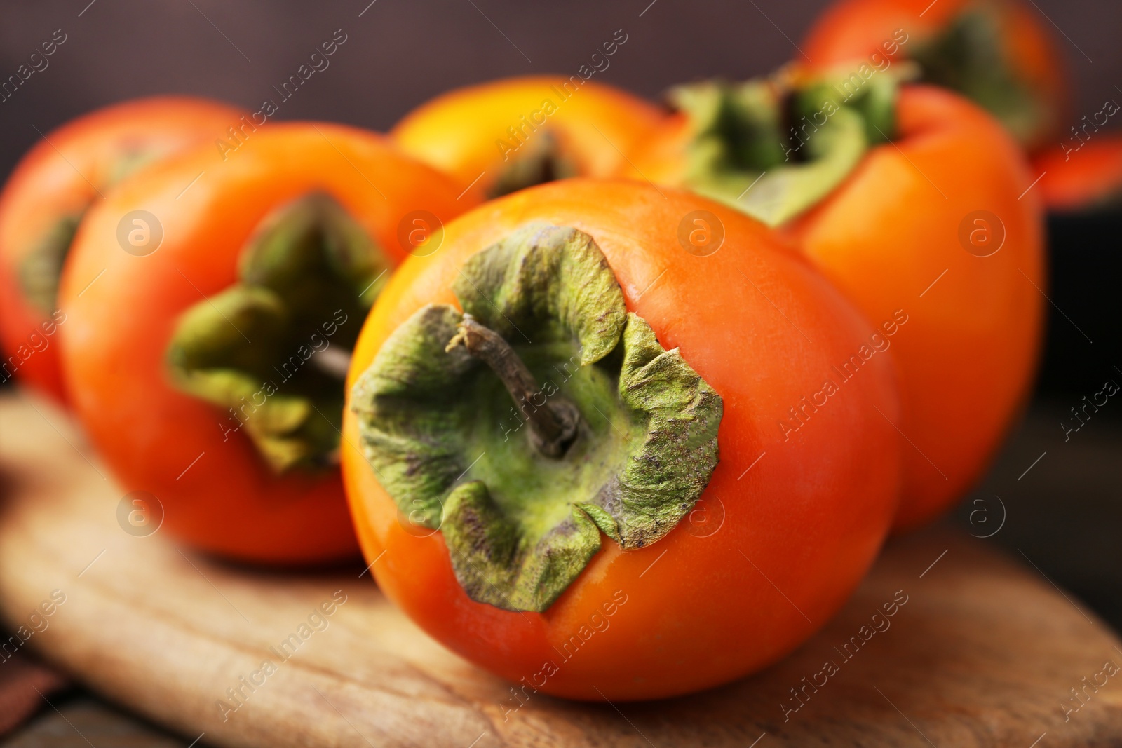 Photo of Delicious fresh juicy persimmons on wooden board, closeup