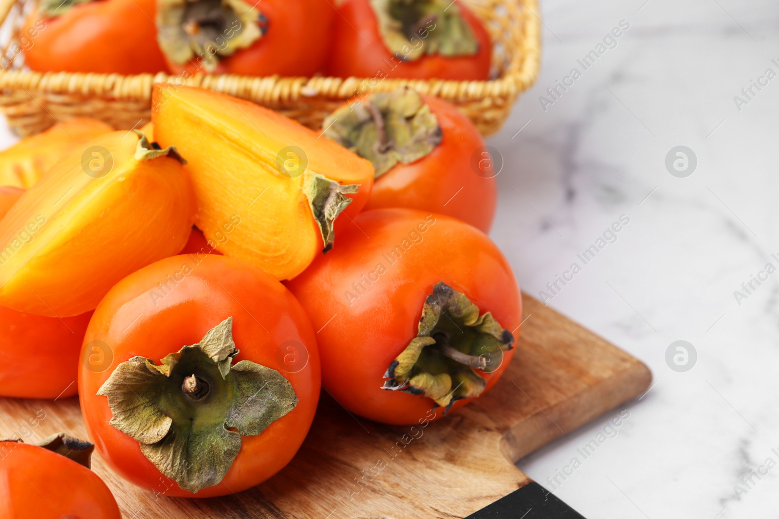 Photo of Whole and cut ripe persimmons on white marble table, closeup