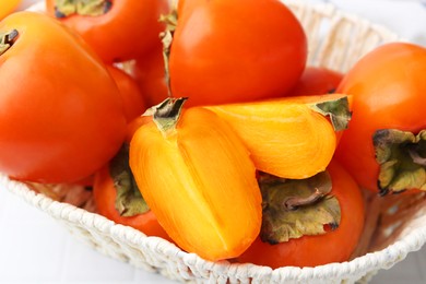 Photo of Ripe persimmons in wicker basket on white table, closeup