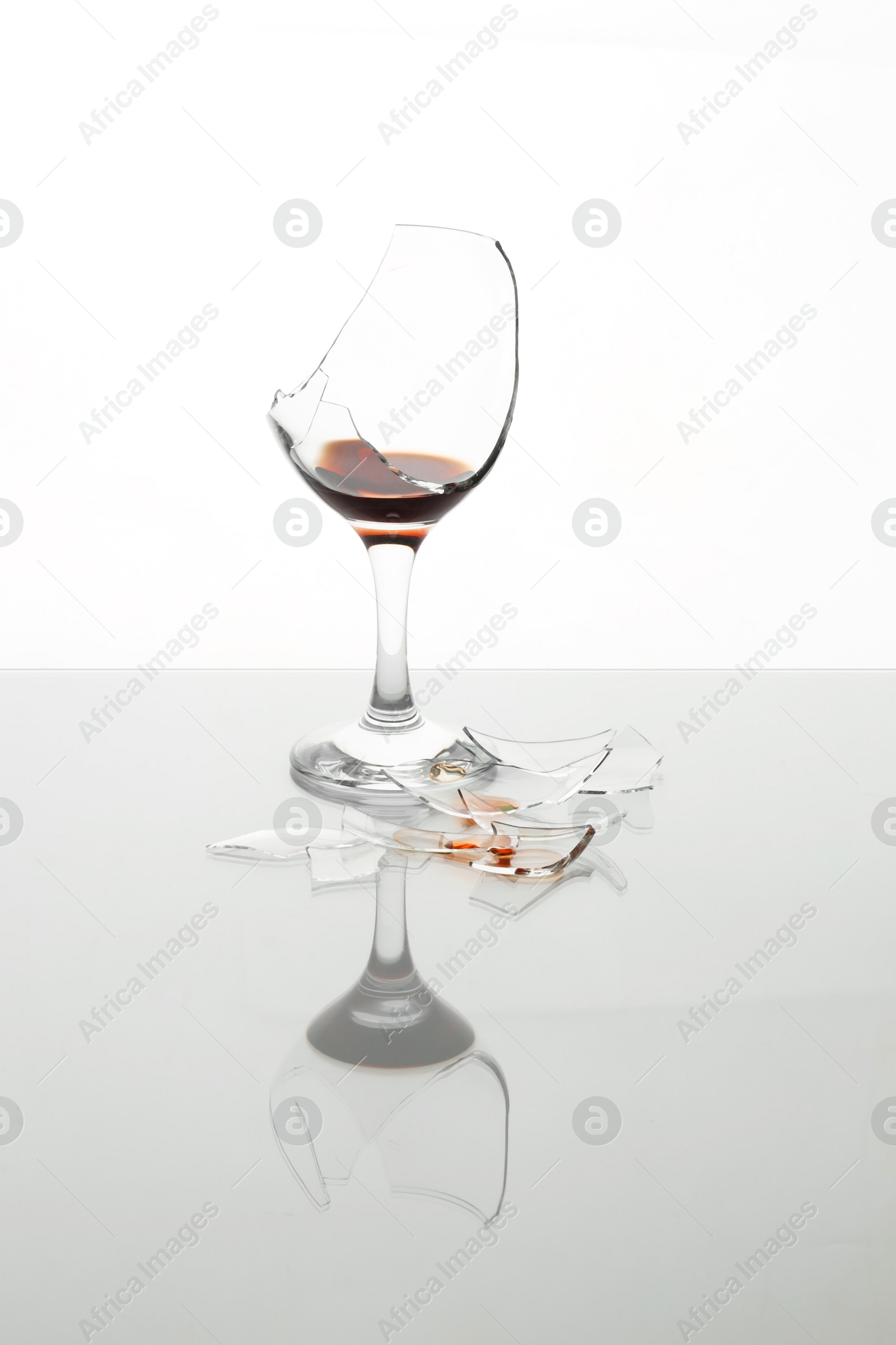 Photo of Pieces of broken glass with wine on table against white background