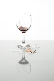 Photo of Pieces of broken glass with wine on table against white background