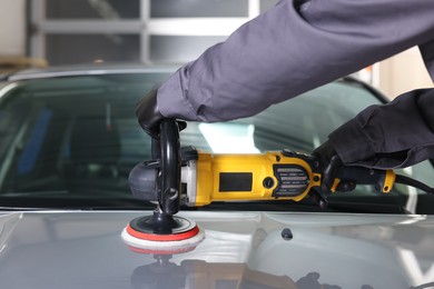 Photo of Man polishing car hood with orbital polisher indoors, closeup