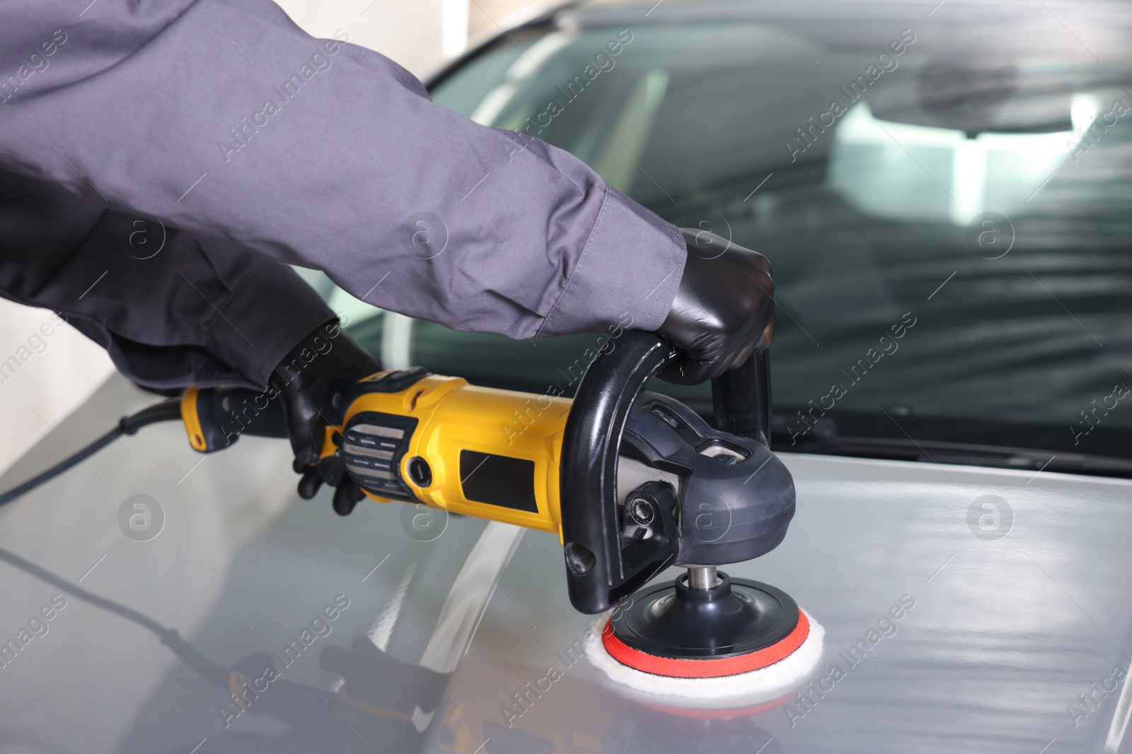 Photo of Man polishing car hood with orbital polisher indoors, closeup