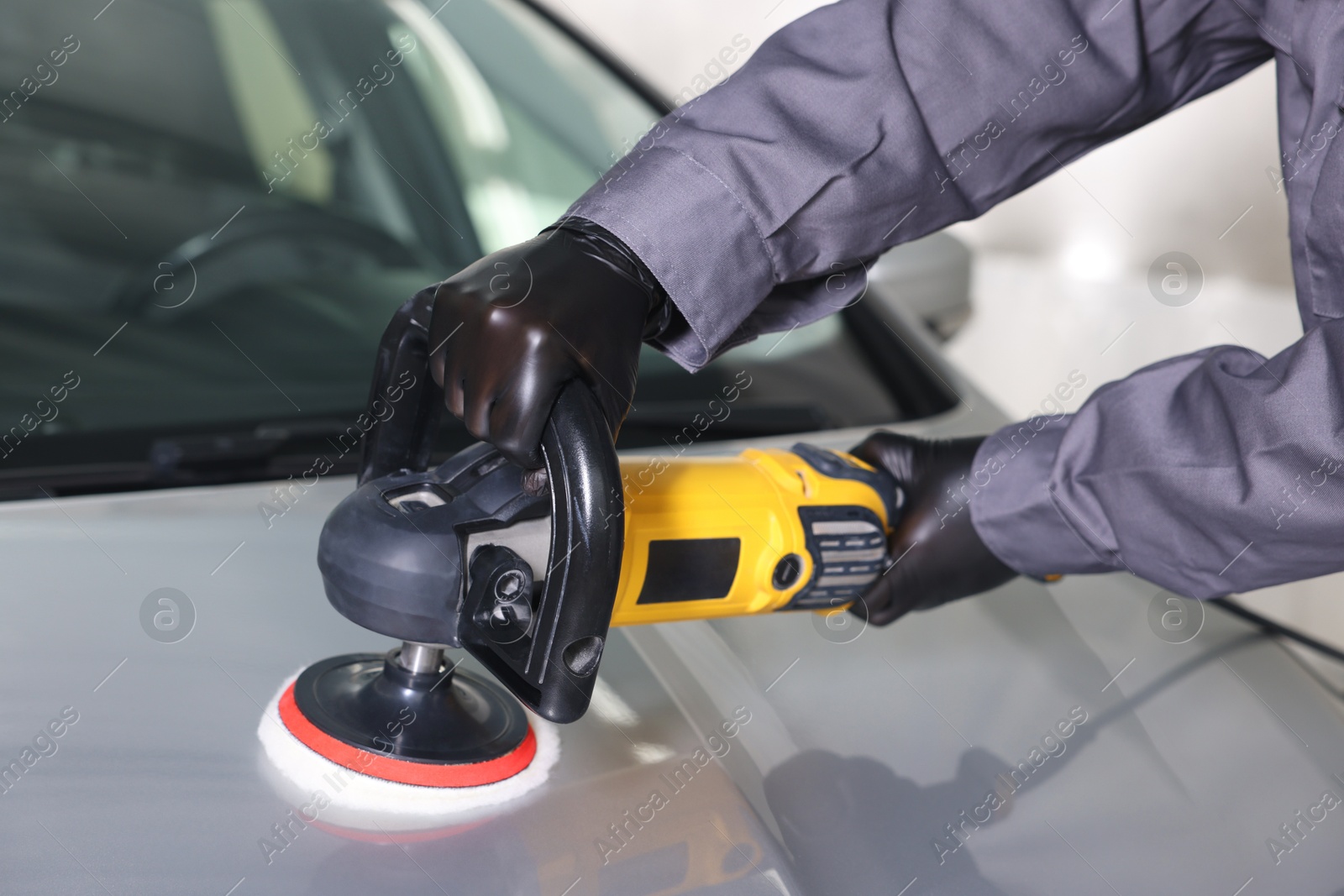 Photo of Man polishing car hood with orbital polisher indoors, closeup