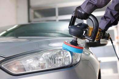 Photo of Man polishing car headlight with orbital polisher indoors, closeup