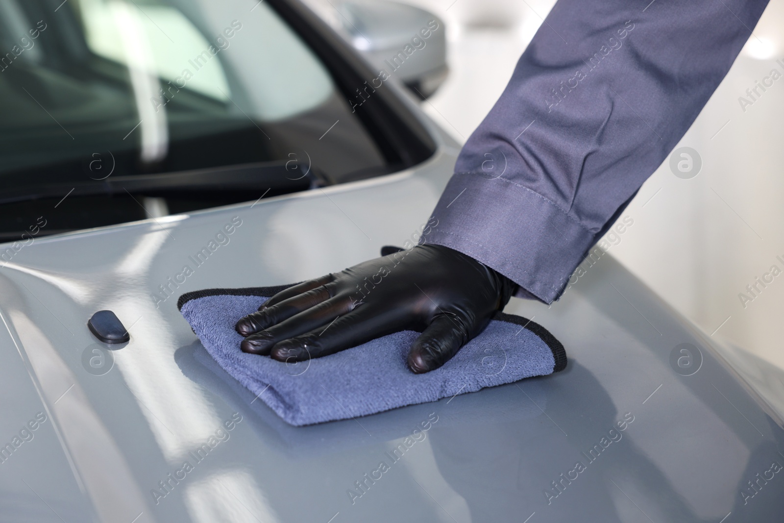 Photo of Man polishing car hood with rag indoors, closeup