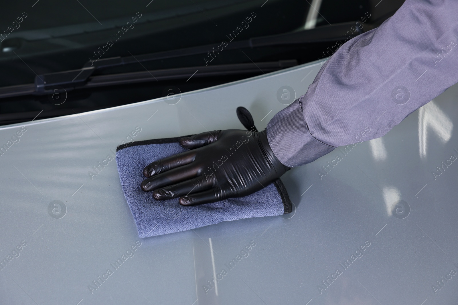 Photo of Man polishing car hood with rag indoors, closeup