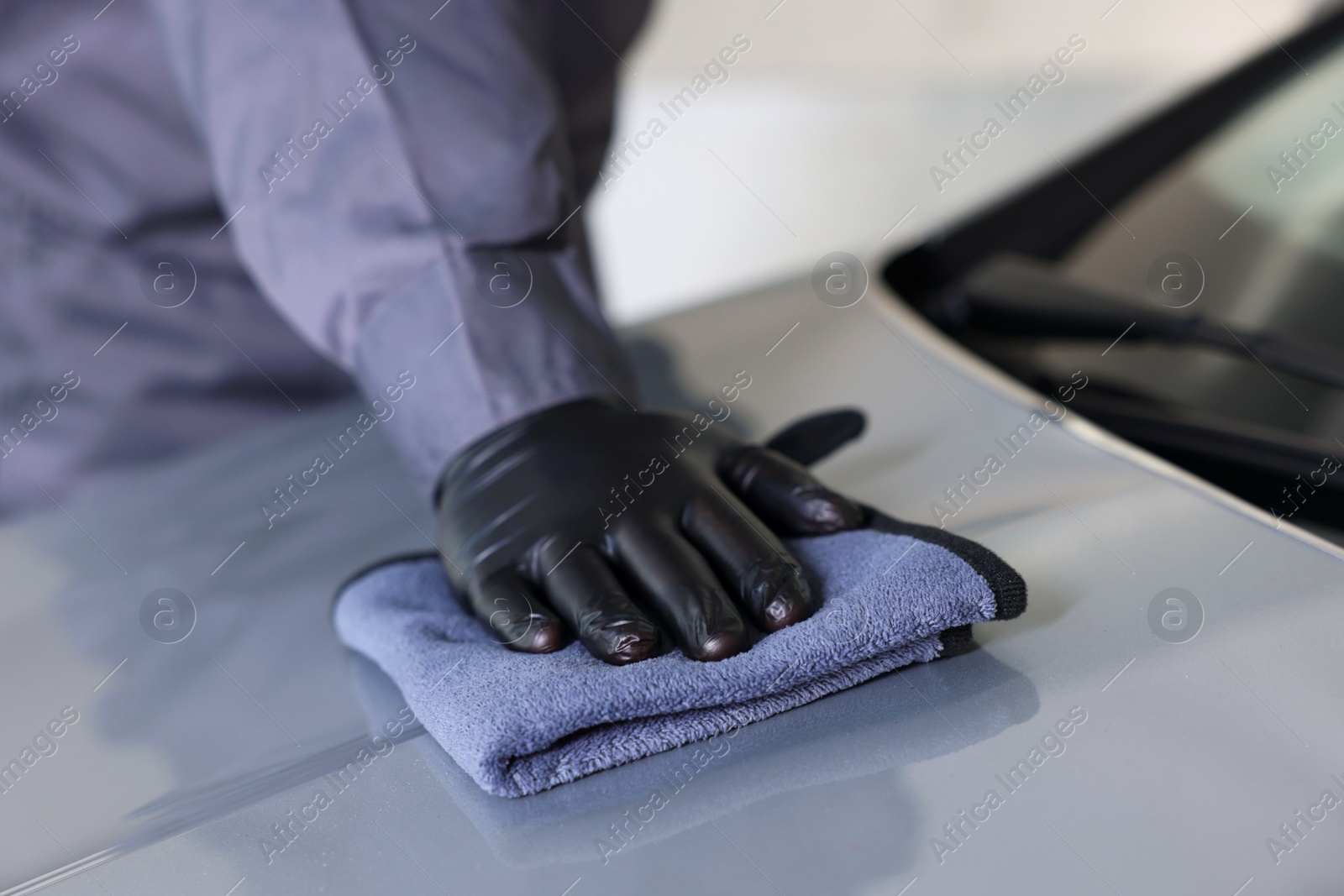 Photo of Man polishing car hood with rag indoors, closeup