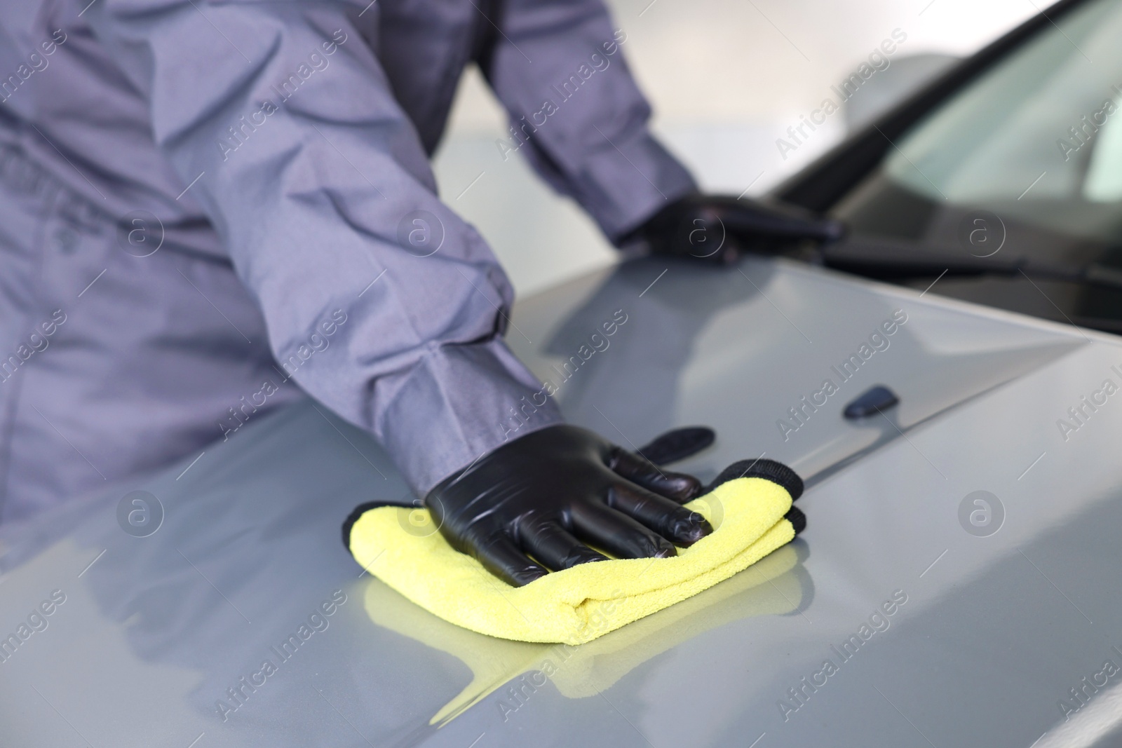 Photo of Man polishing car hood with rag indoors, closeup