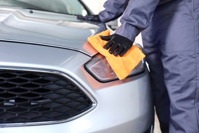 Photo of Man polishing car headlight with orange rag indoors, closeup