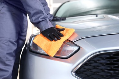 Photo of Man polishing car headlight with orange rag indoors, closeup