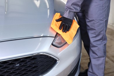 Photo of Man polishing car headlight with orange rag indoors, closeup