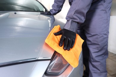 Photo of Man polishing car headlight with orange rag indoors, closeup