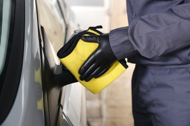 Photo of Man cleaning car side view mirror with yellow rag indoors, closeup