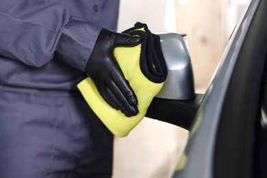 Photo of Man cleaning car side view mirror with yellow rag indoors, closeup