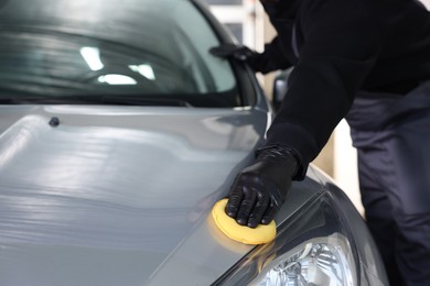 Photo of Man polishing car hood with yellow sponge indoors, closeup