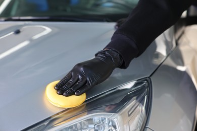 Photo of Man polishing car hood with yellow sponge indoors, closeup