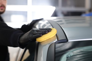 Photo of Man polishing car with yellow sponge indoors, closeup