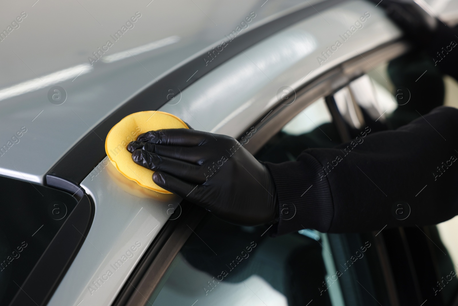 Photo of Man polishing car with yellow sponge indoors, closeup