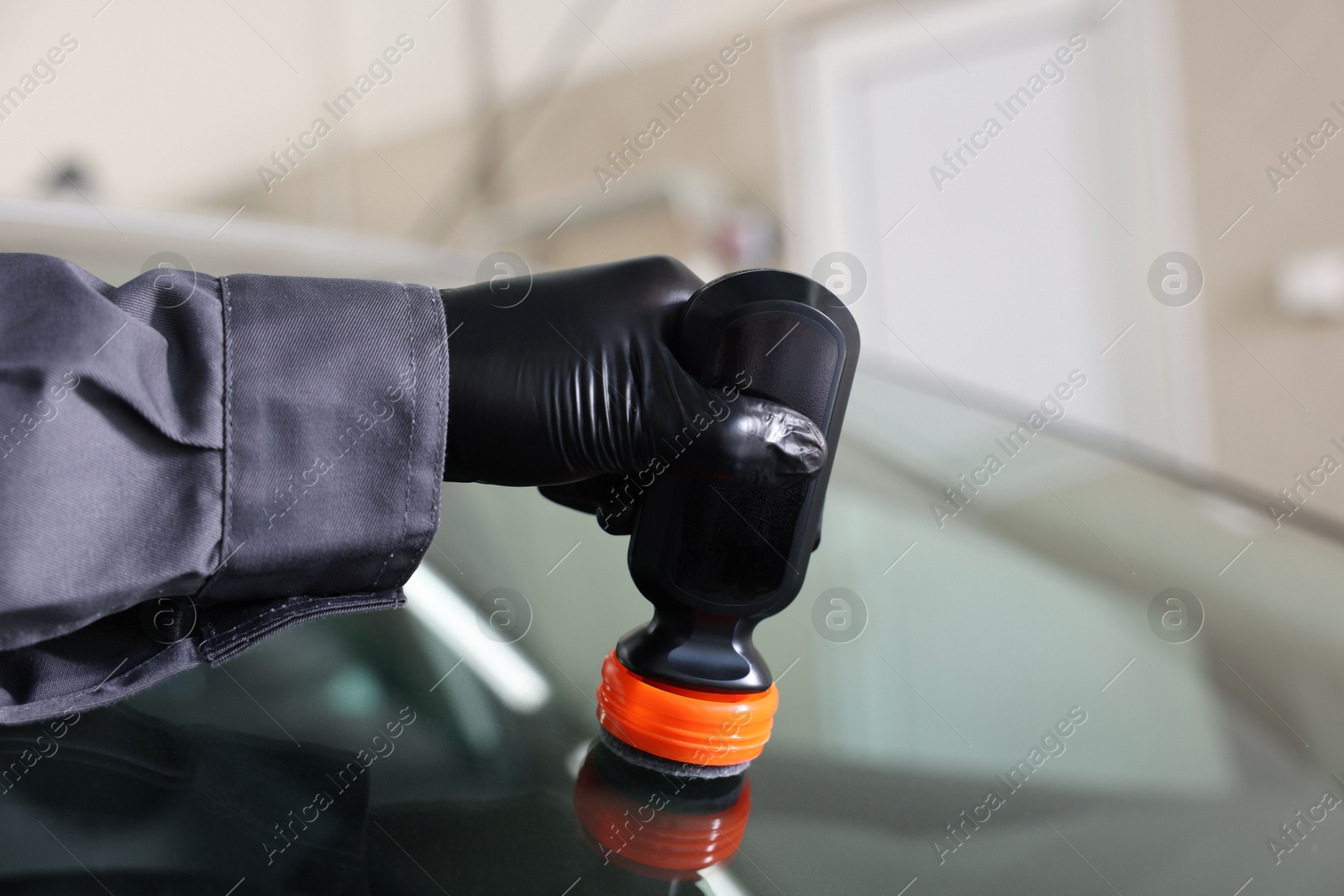 Photo of Man polishing car windshield indoors, closeup view