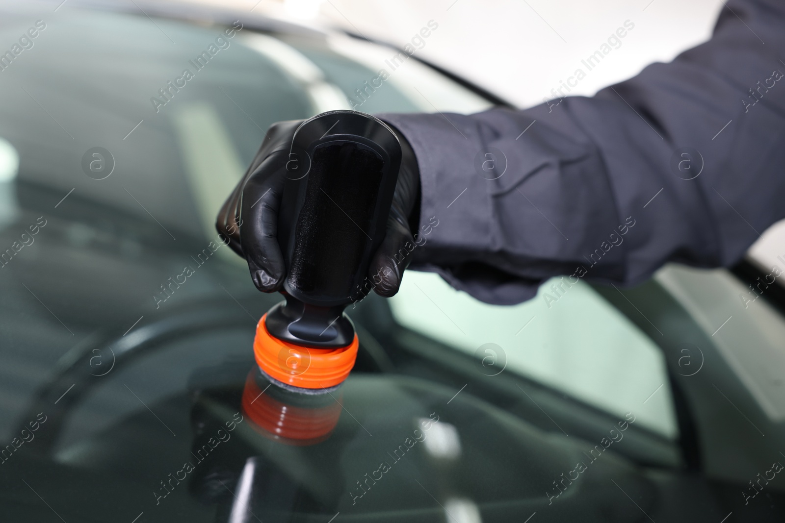 Photo of Man polishing car windshield indoors, closeup view