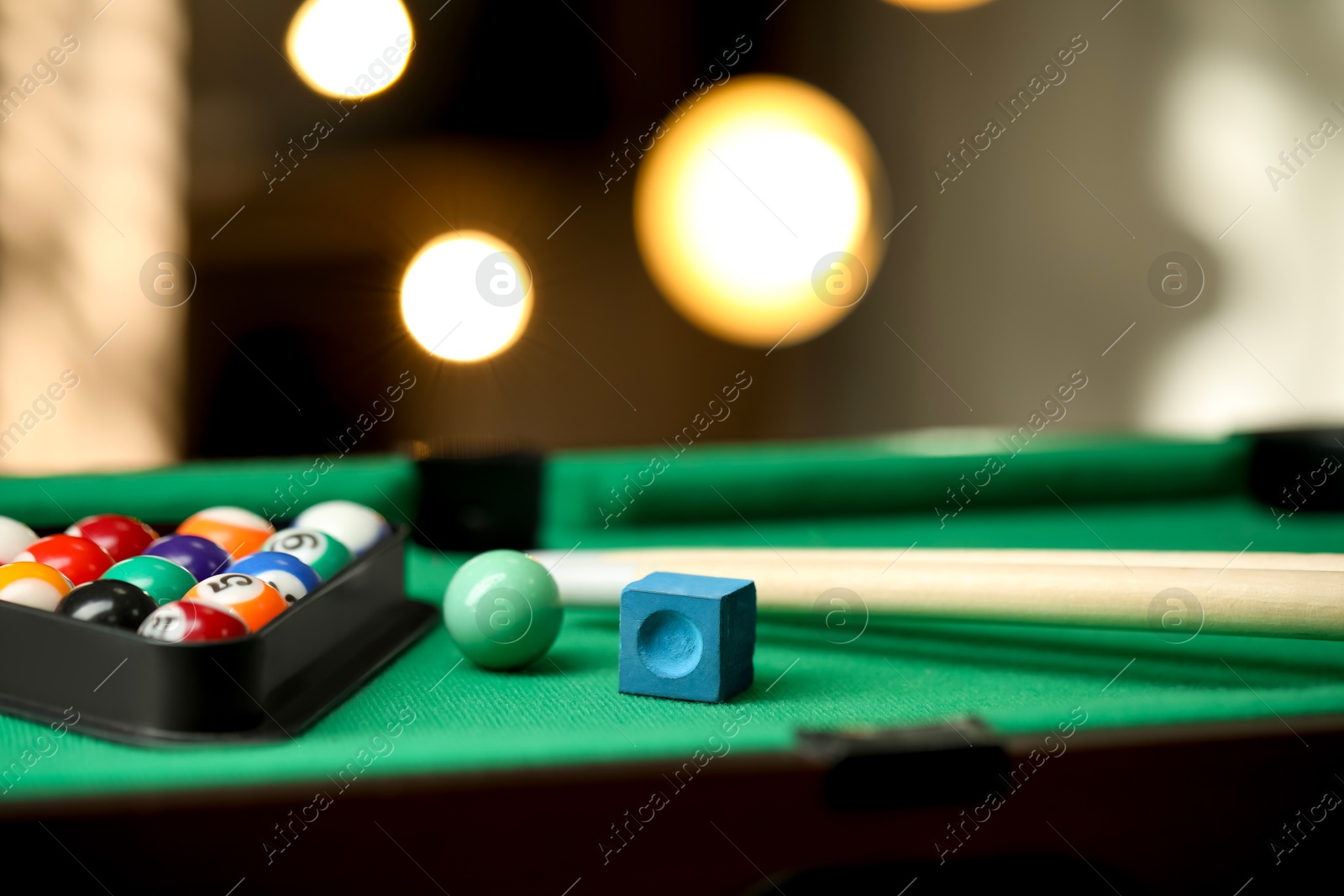 Photo of Many colorful billiard balls in triangle rack, cues and chalk on green table indoors, closeup