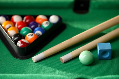 Photo of Many colorful billiard balls in triangle rack, cues and chalk on green table, closeup