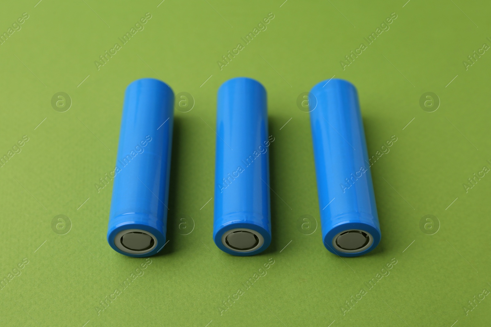 Photo of Three AA cell batteries on green background, closeup