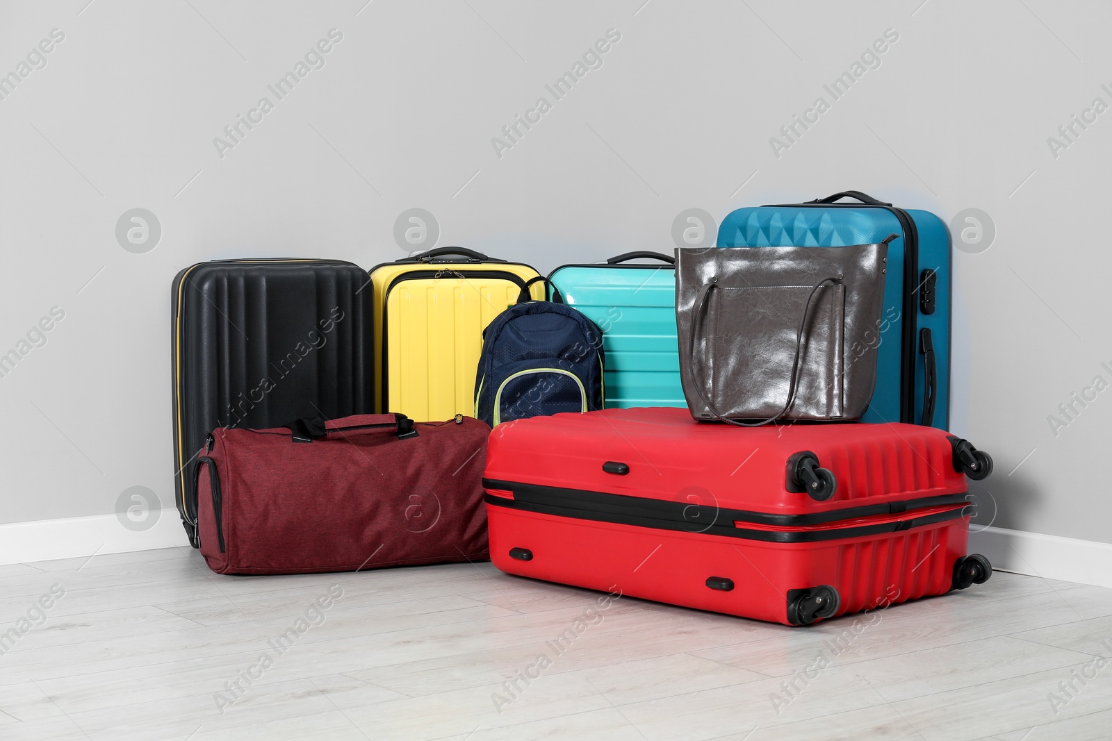 Photo of Colorful suitcases, backpack and bags on floor near light wall