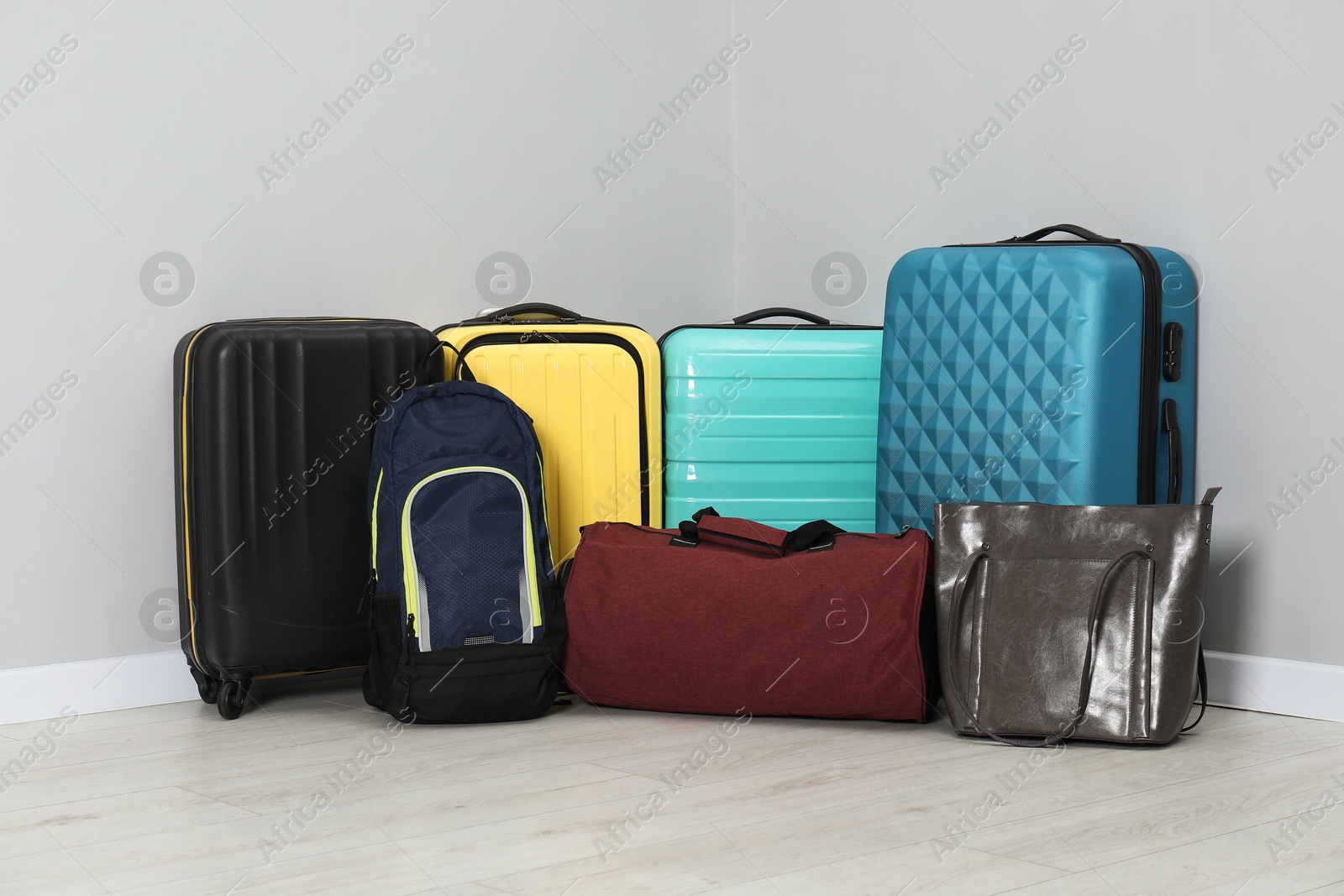 Photo of Colorful suitcases, backpack and bags on floor near light wall