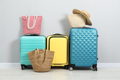 Photo of Colorful suitcases, beach bags and straw hat on floor near light wall