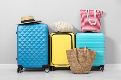 Photo of Colorful suitcases, beach bags and straw hat on floor near light wall