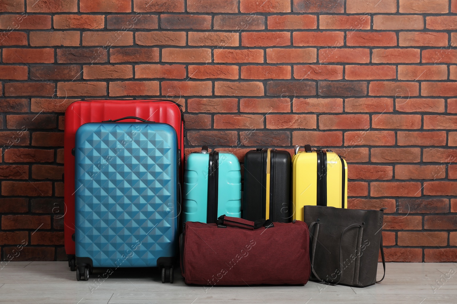 Photo of Many colorful suitcases and bags on floor near brick wall