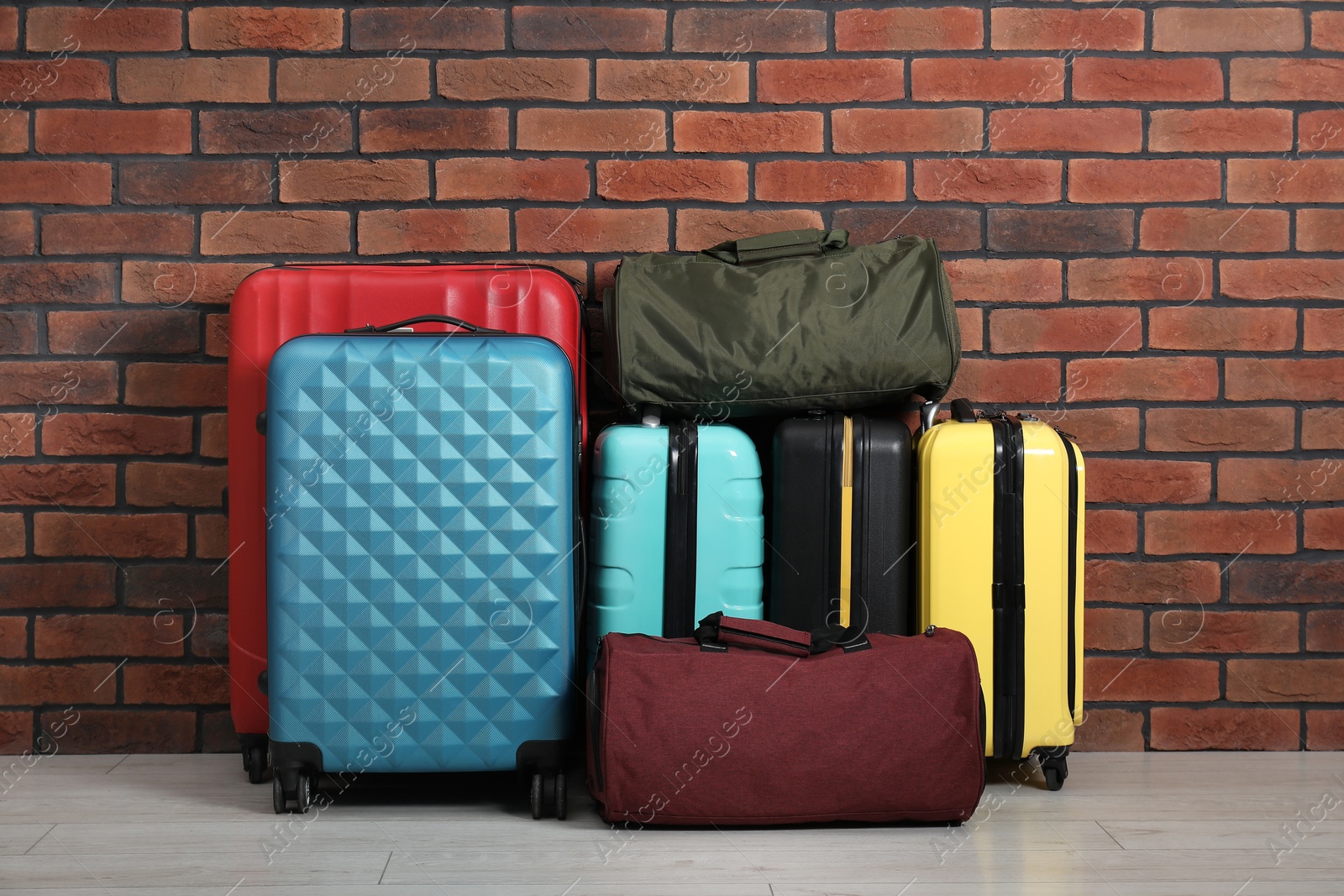 Photo of Many colorful suitcases and bags on floor near brick wall