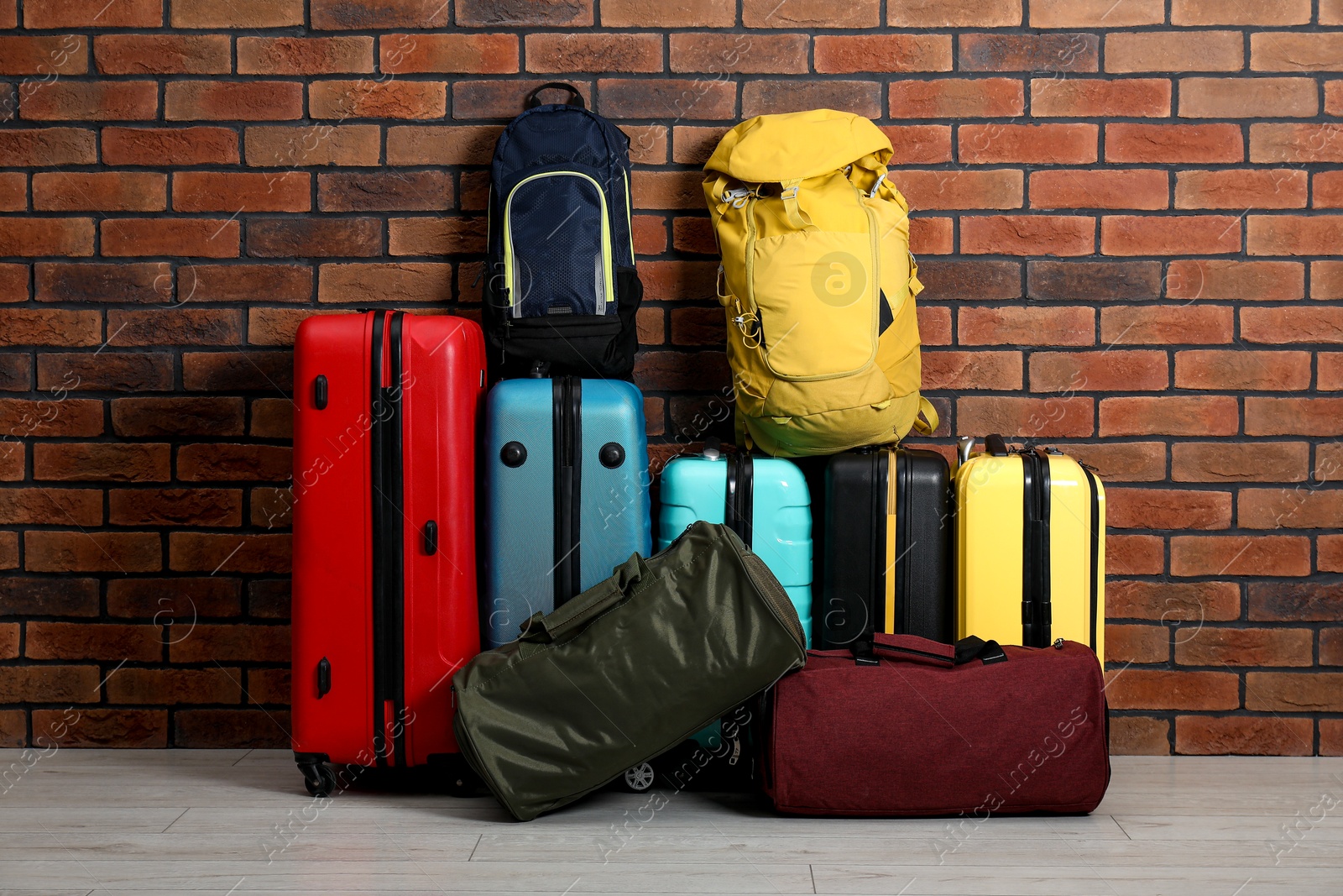 Photo of Many colorful suitcases, backpacks and bags on floor near brick wall