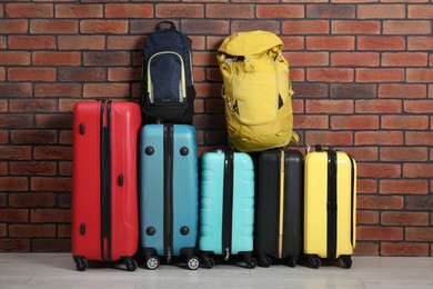 Photo of Many colorful suitcases and backpacks on floor near brick wall