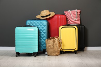 Photo of Colorful suitcases, beach bags and hat on floor near black wall