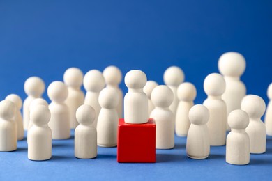 Photo of Competition concept. Human figure on wooden cube and other ones behind against blue background, closeup