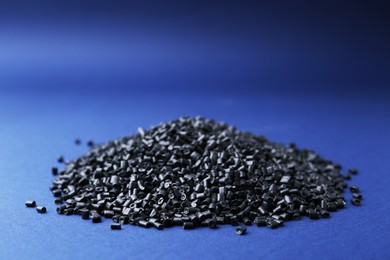 Photo of Pile of black plastic granules on blue background, closeup